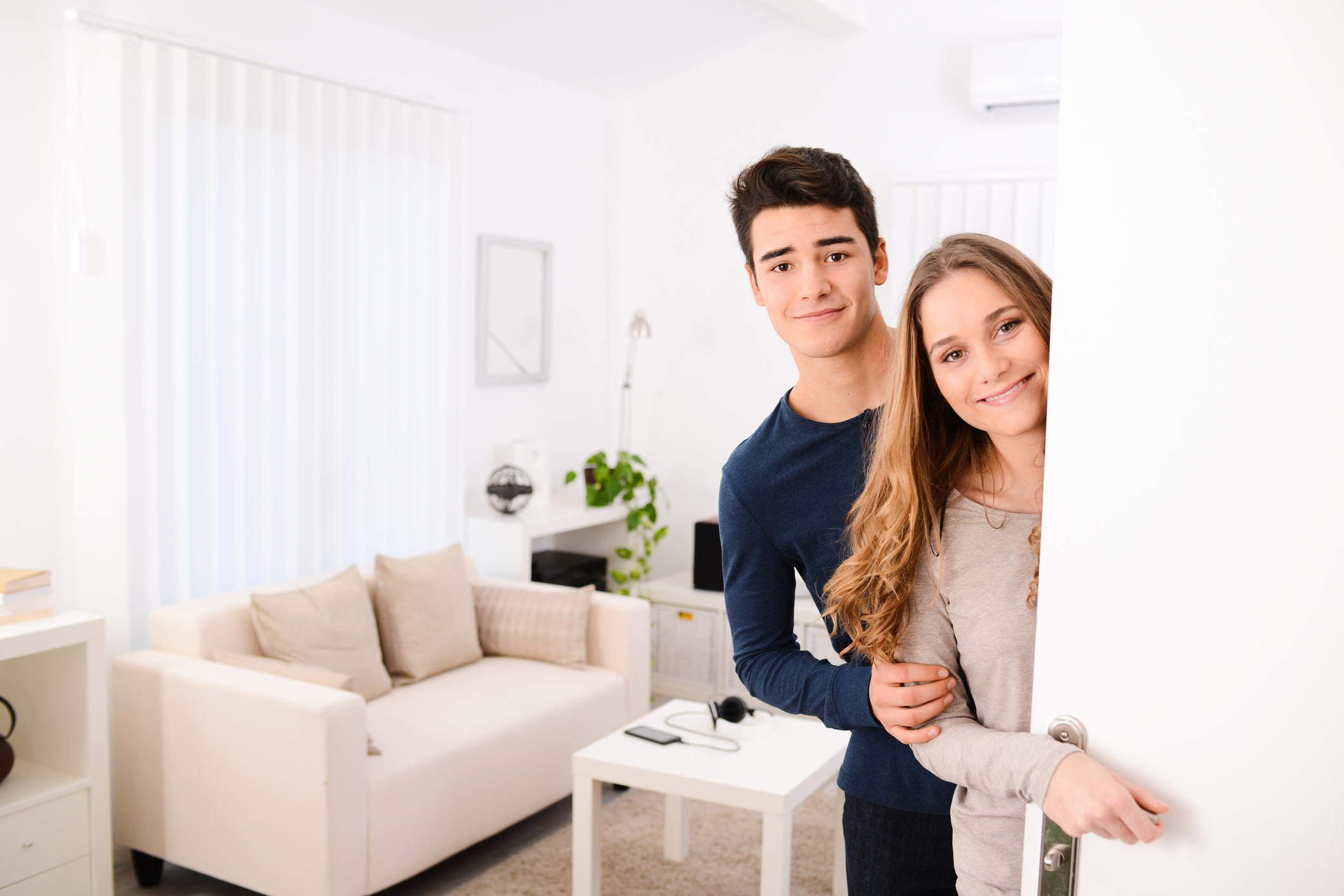 happy young couple opening door and welcoming friends apartment